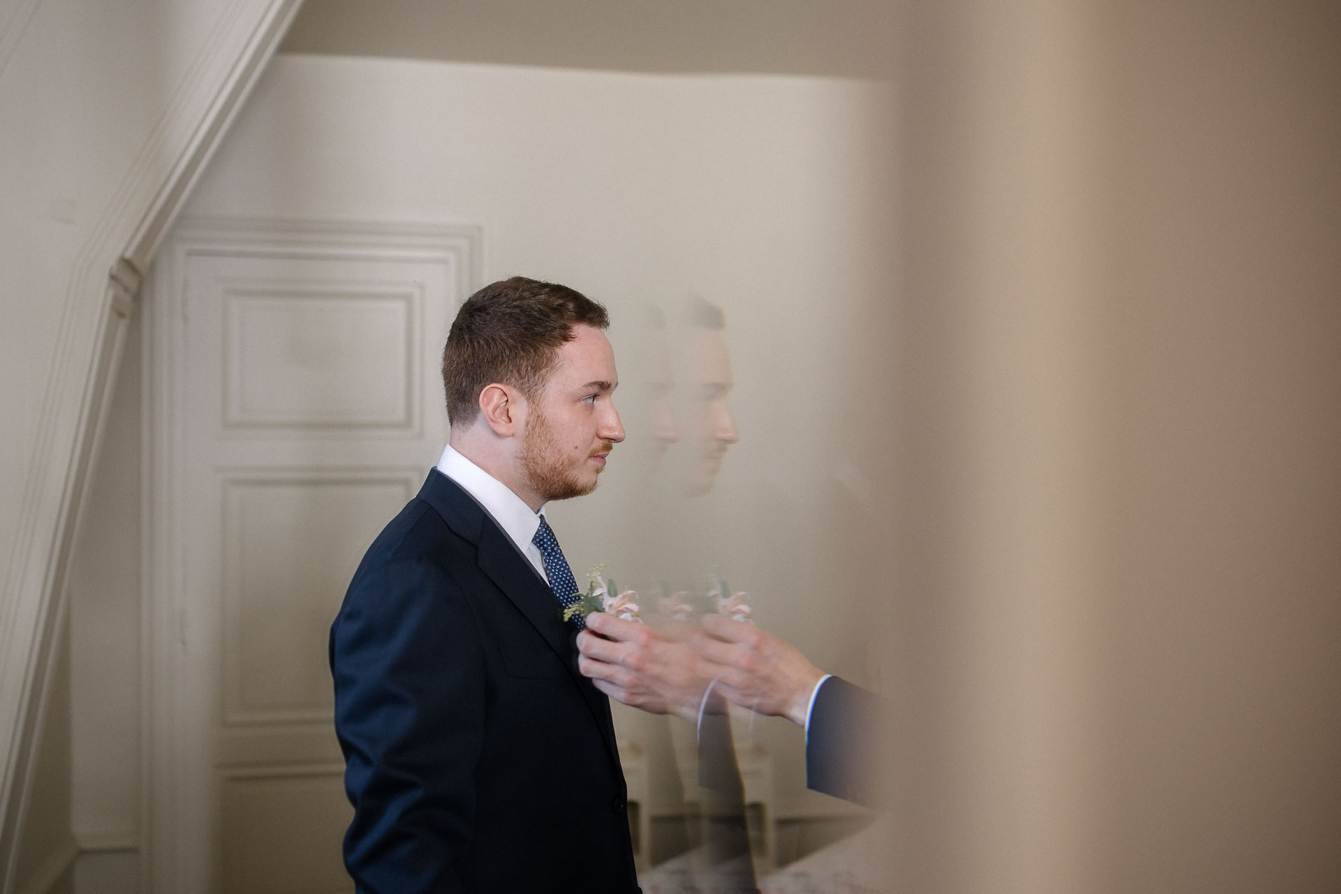 Portrait du marié en train de mettre sa boutonnière, reflet dans le miroir