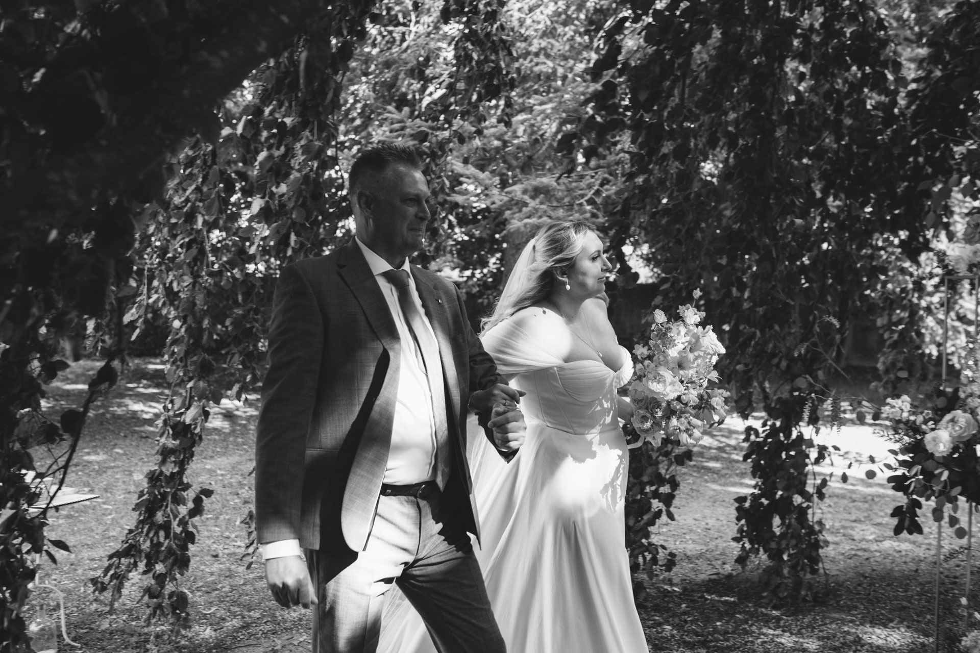 La mariée marchant vers l’autel au bras de son père, entourée de verdure