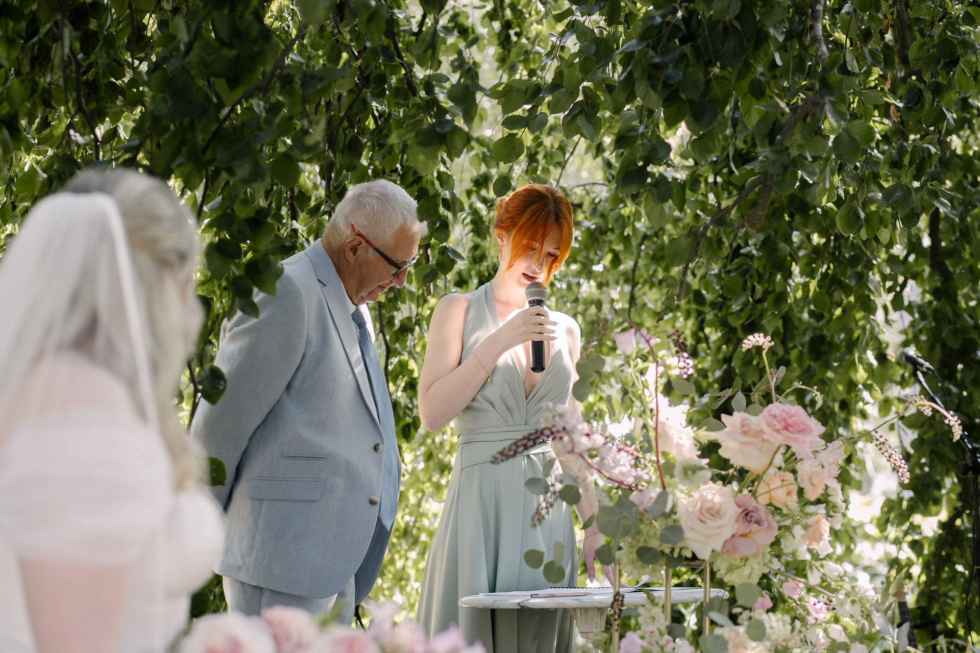 Discours d’une demoiselle d’honneur accompagné d’un homme plus âgé, dans un décor végétal