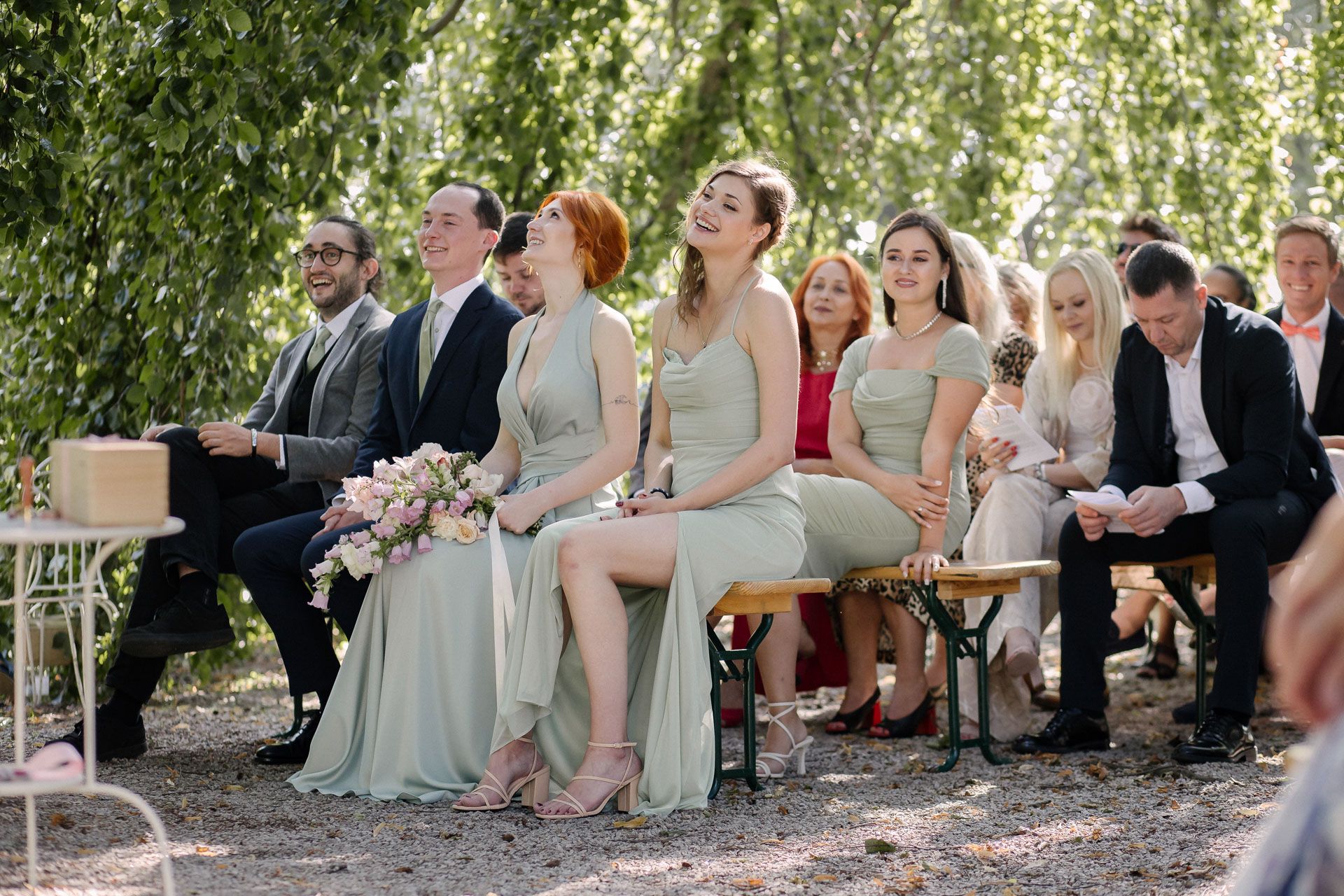Invités et demoiselles d’honneur souriants, assis sous des branches lors de la cérémonie