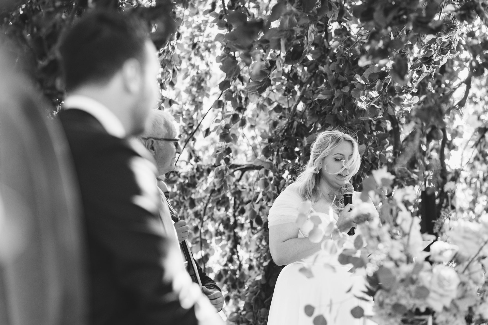 La mariée lisant un discours pendant la cérémonie, sous un feuillage dense