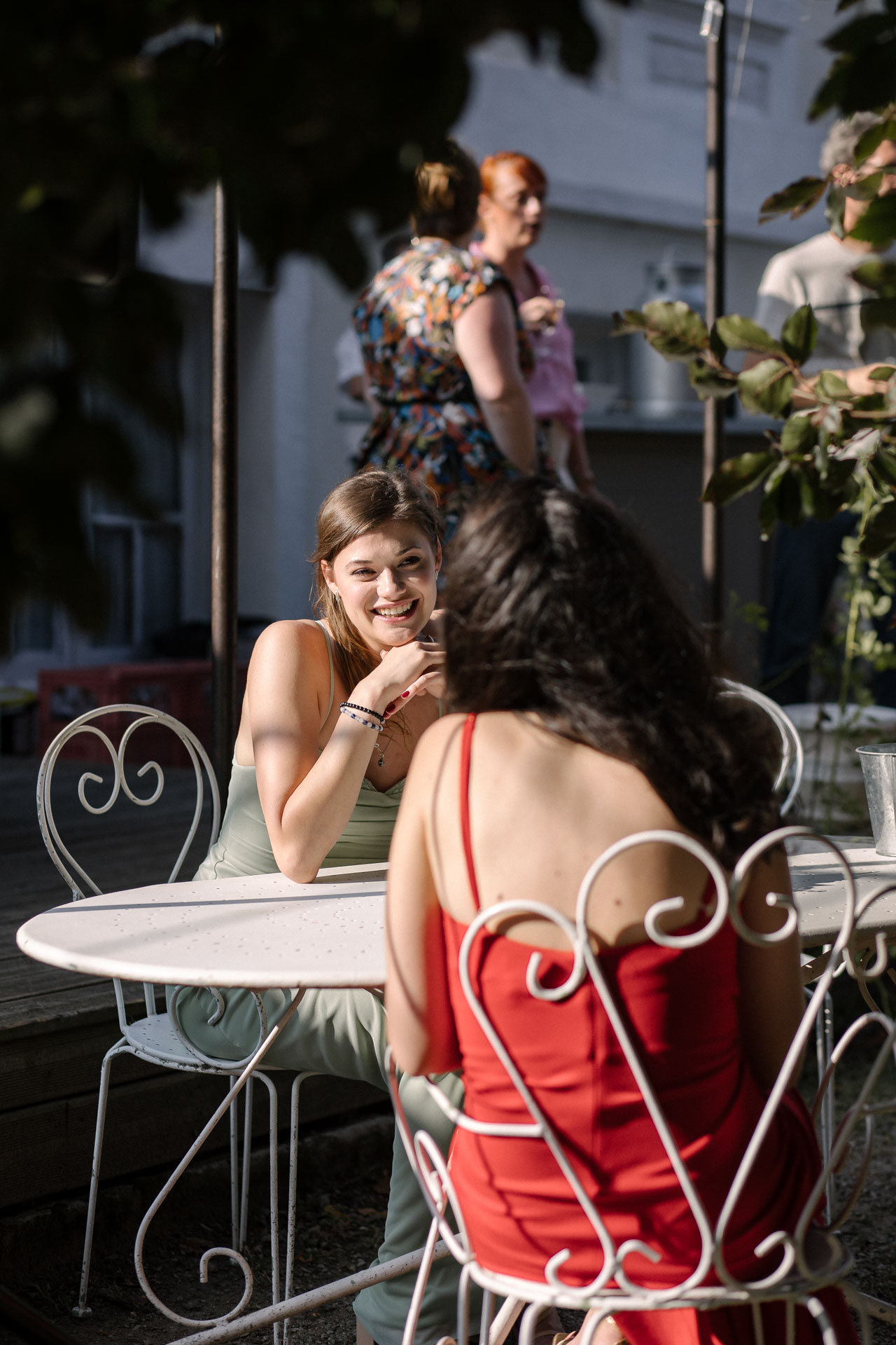 Conversation joyeuse entre deux invitées assises à une table de jardin en fer forgé