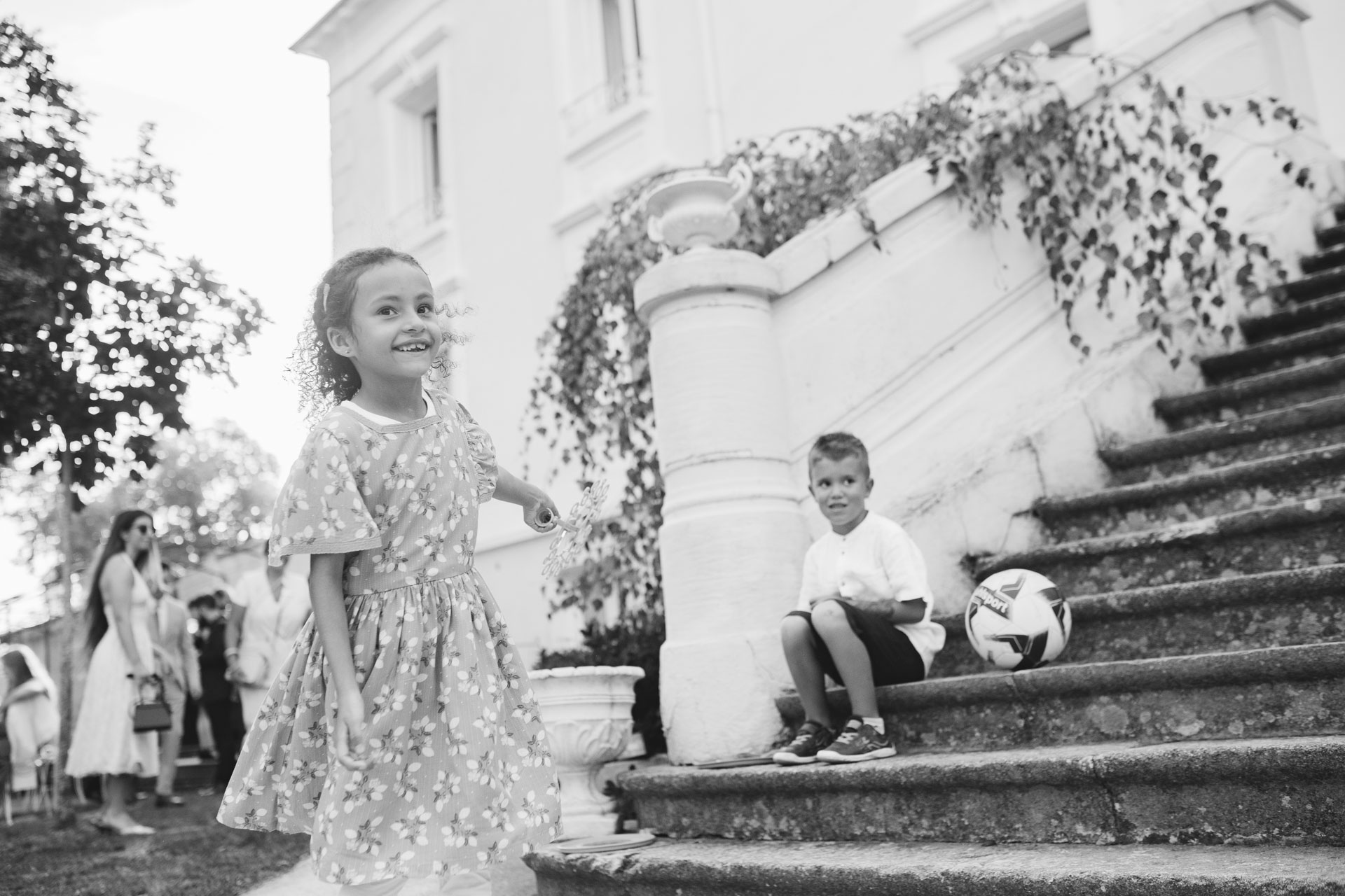 Deux enfants jouent autour d’un escalier en pierre pendant le mariage, une fille souriante en robe fleurie et un garçon avec un ballon