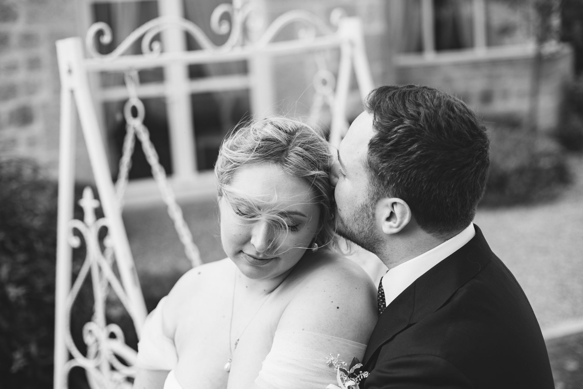 Photo en noir et blanc du marié embrassant le front de la mariée, moment intime dans les jardins