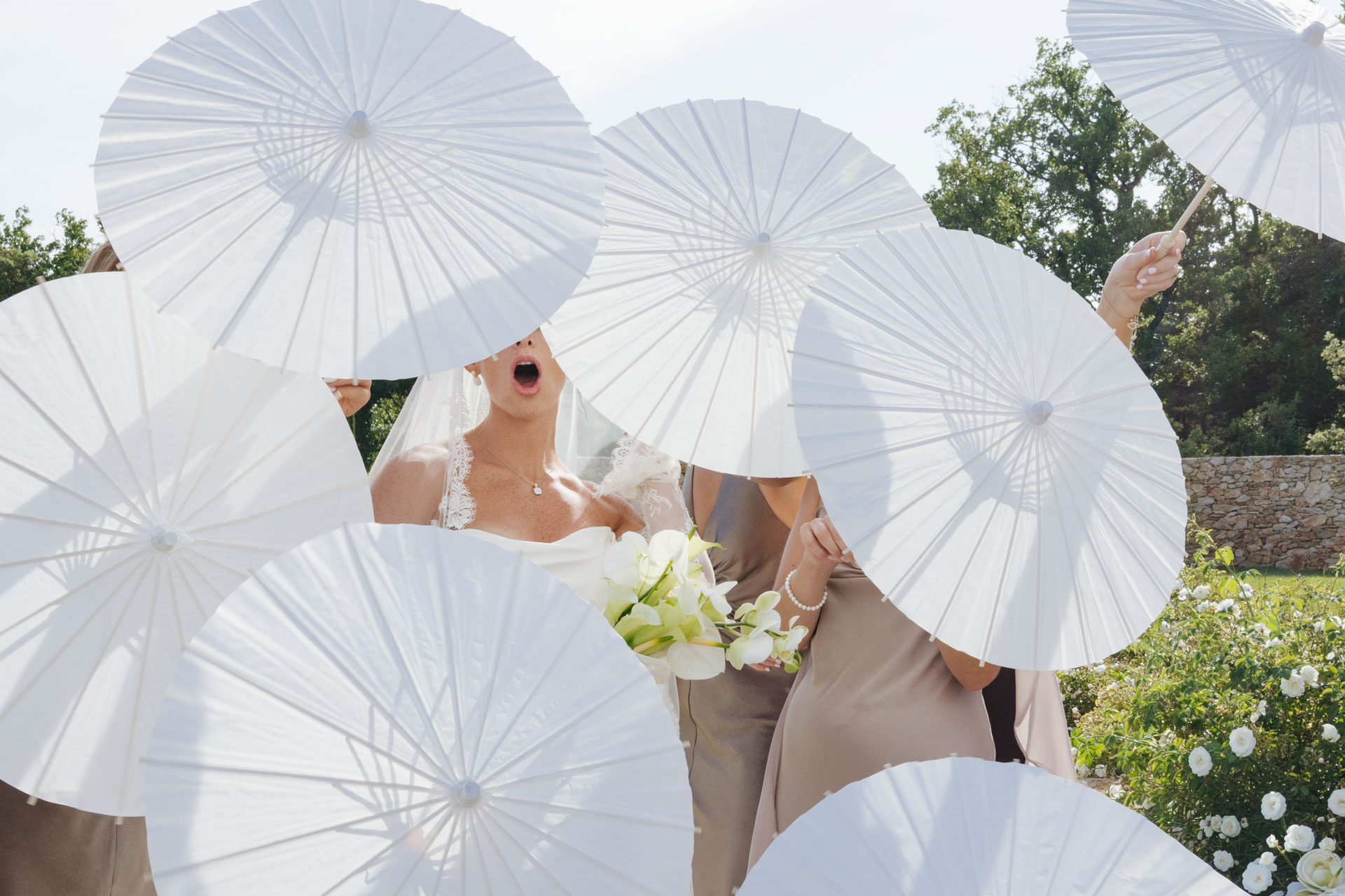 Bride laughing among white parasols at cocktail hour — Grange de Javon wedding