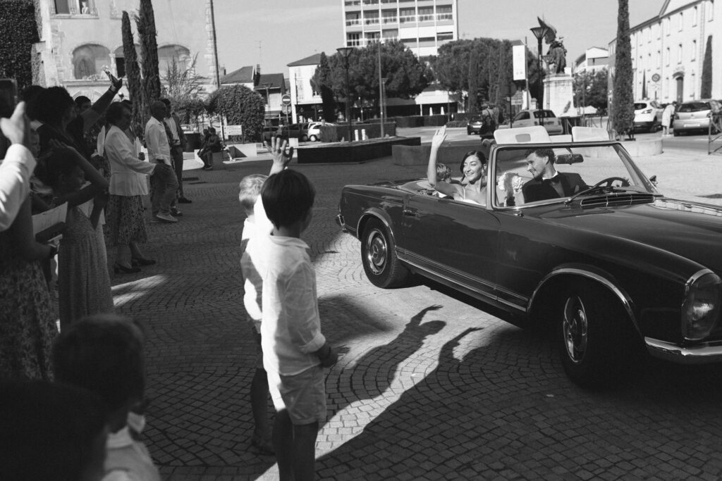 Mariés saluant leurs invités depuis une voiture décapotable vintage
