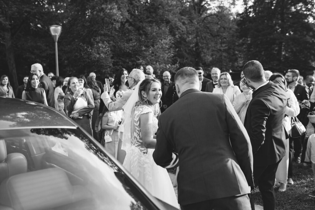 Mariée souriante entourée de ses invités avant le départ en voiture