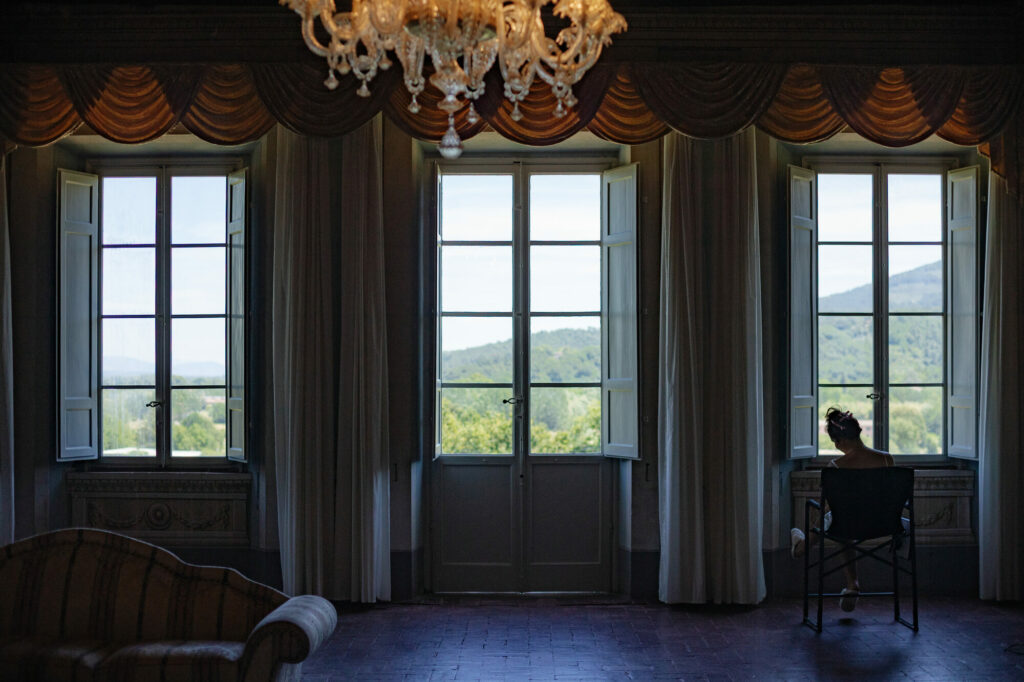 Bride silhouetted at a window overlooking the Tuscan hills