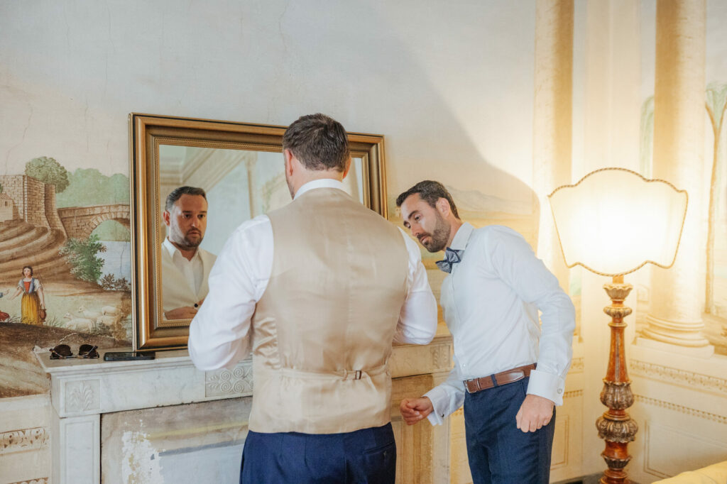 Groom and best man getting ready beneath frescoed ceilings
