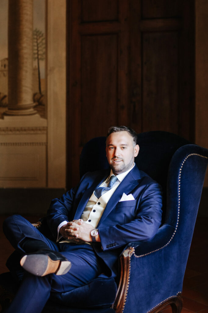 Portrait of the groom seated in a blue velvet armchair